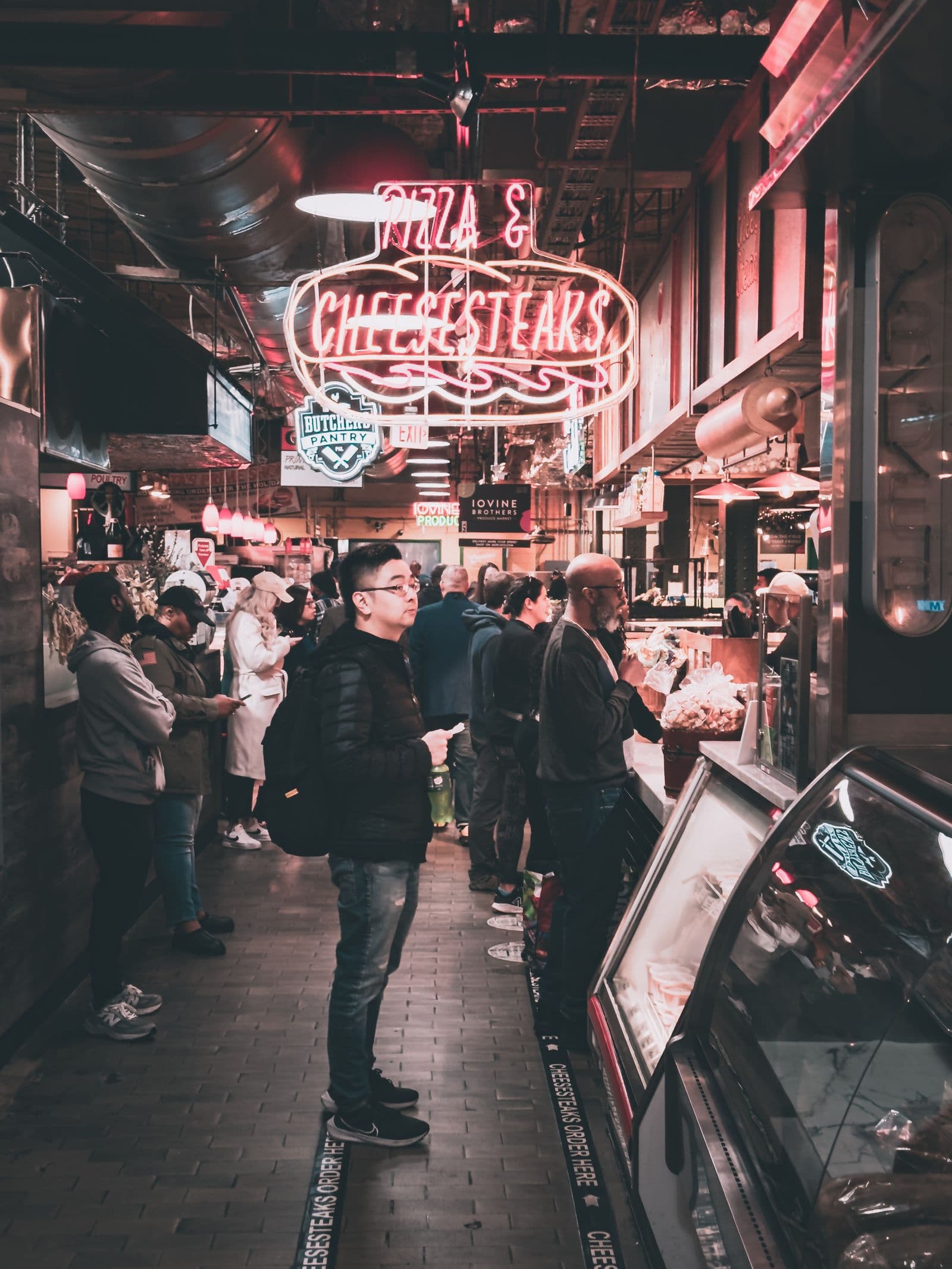 A crowd lined up at neon-lit food stalls inside a busy indoor market