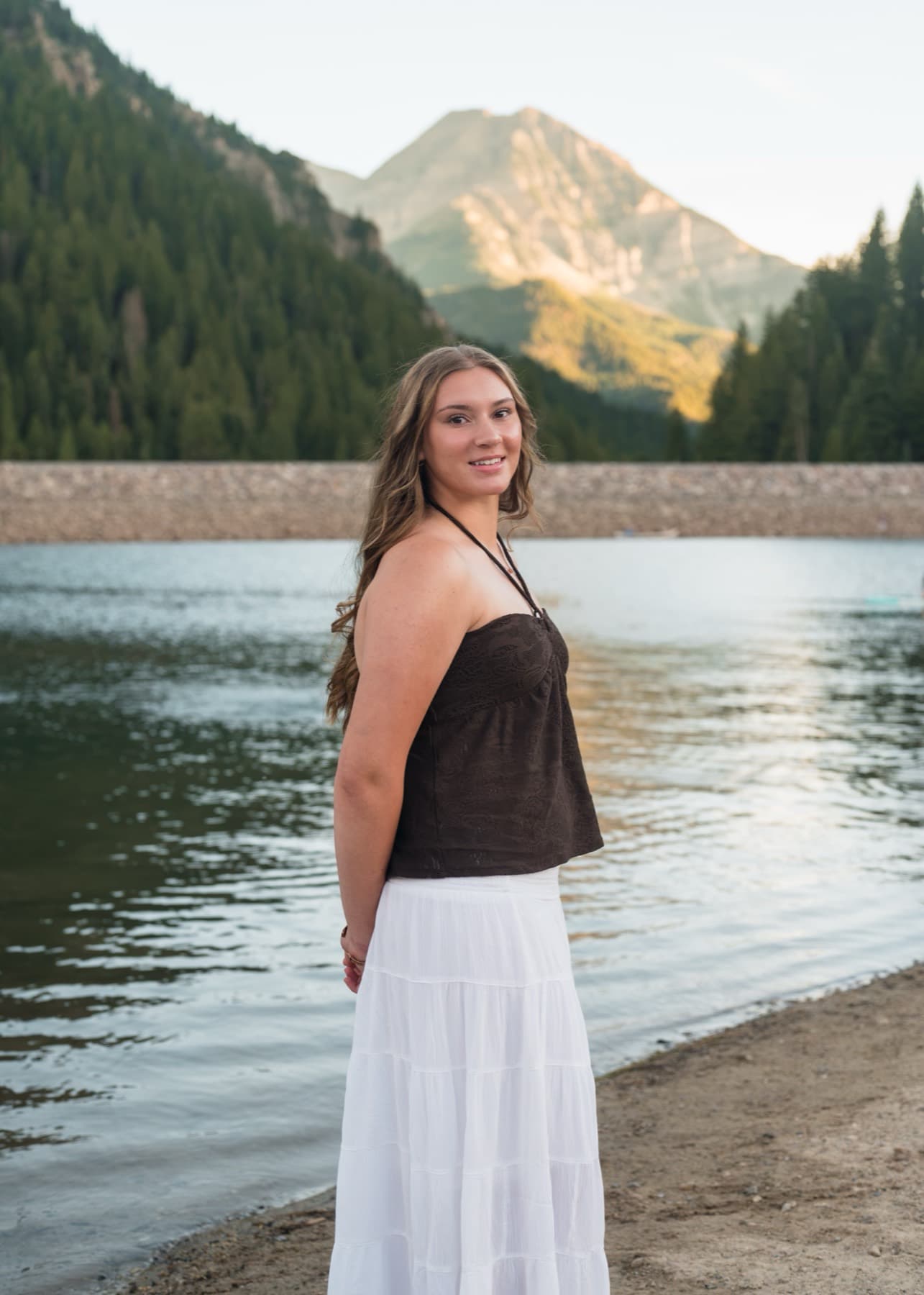 Senior at a mountain lake, looking back over her shoulder at golden hour