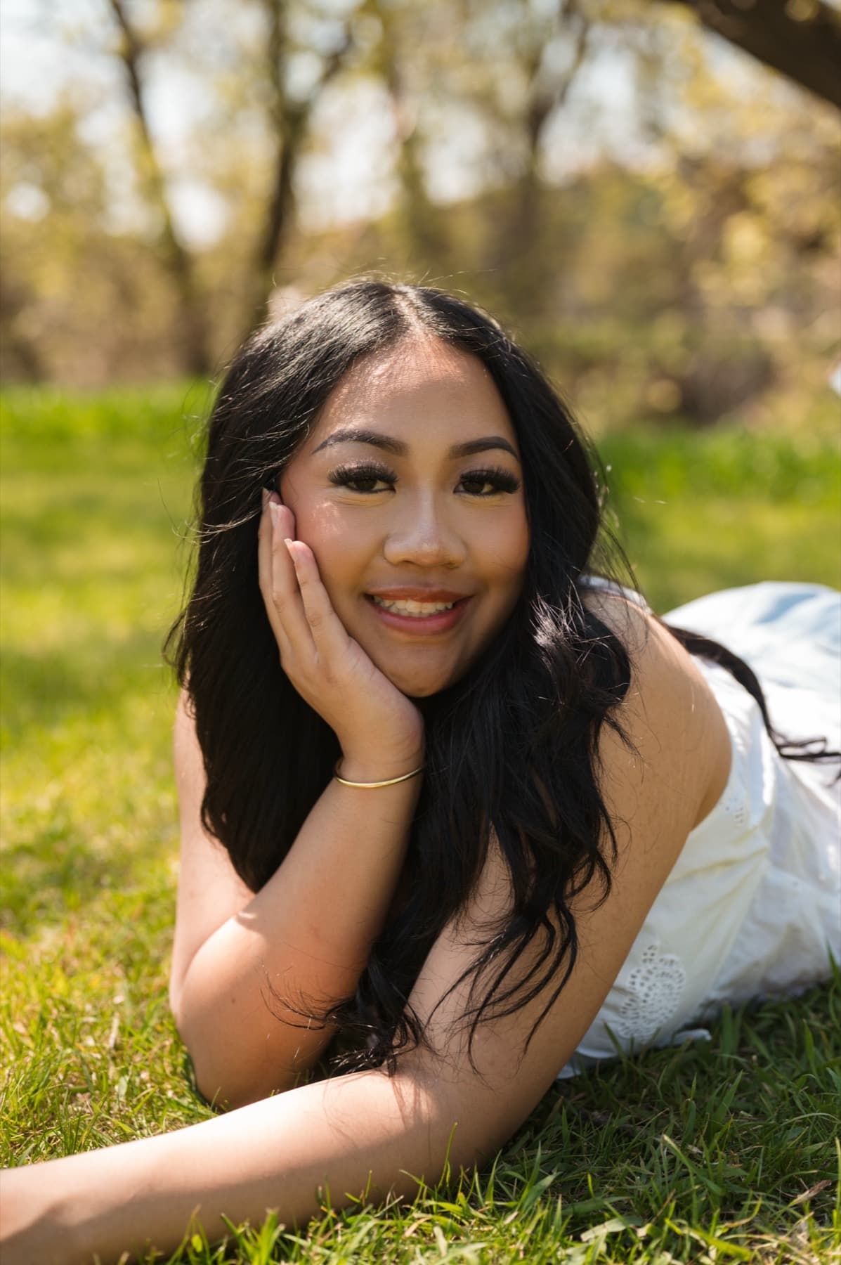 Senior lying in the grass under spring trees, chin in her hand