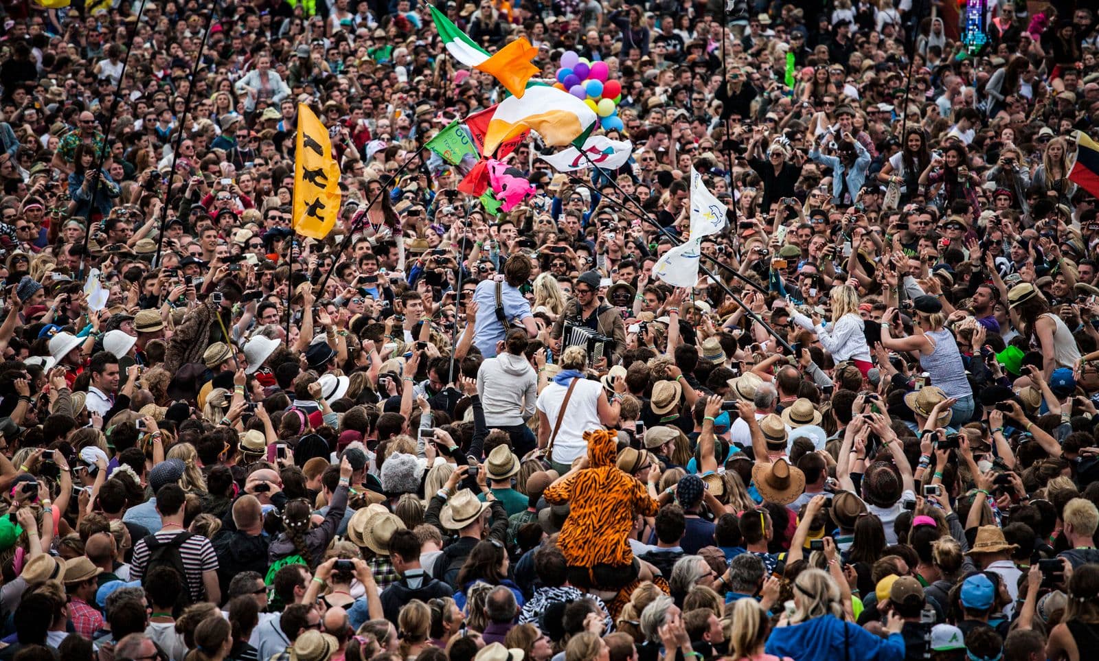 A packed festival crowd waving flags around a band playing among them