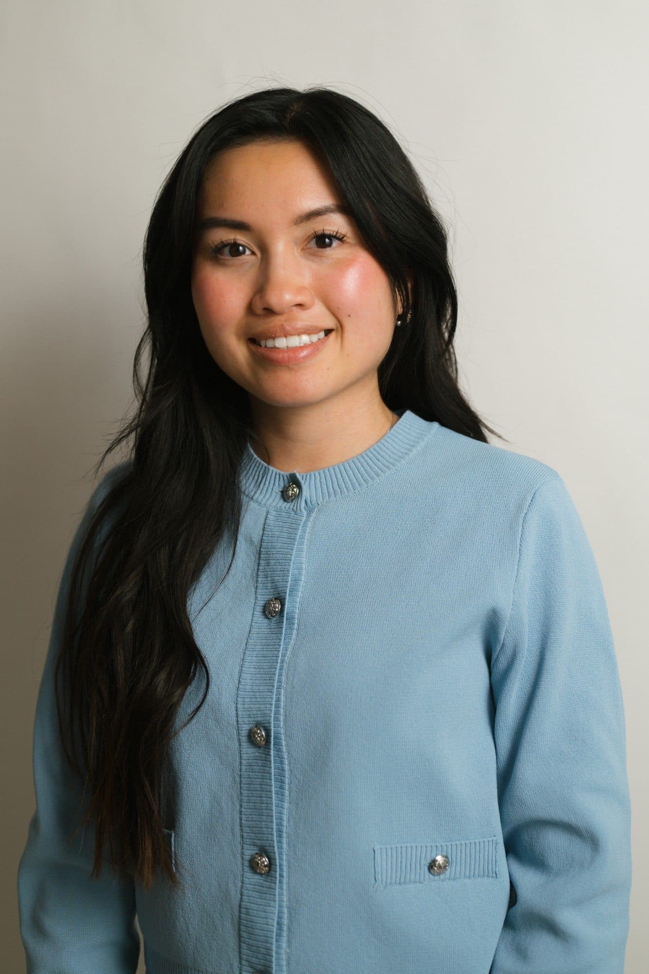 Angel Phommachan smiling in a light blue cardigan against a plain wall